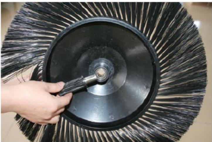 Close-up of a hand using a tool to clean or brush the blade of a black circular object (no text or symbols visible)