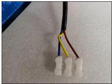Close-up of a white plastic connector with three white terminal pins connected by wires (black, blue, yellow) against a textured white background.