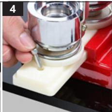 Close-up of a hand using a metal tool to press or install a small cylindrical object on a red surface (no visible text or symbols)