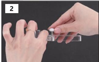 Close-up of hands holding a small white object with a transparent container, against a dark background (no text or symbols visible)