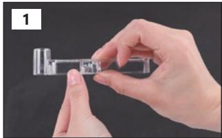 Close-up of hands holding a small transparent object with a small inset, against a dark background (no text or symbols visible)