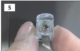 Close-up of a hand holding a small transparent plastic electronic component with a central screw (no visible text or symbols)
