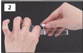 Close-up of hands holding a small white object with a transparent container, against a dark background (no text or symbols visible)