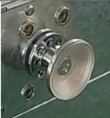Close-up of a mechanical component with a metallic housing and bolts, resting on a green surface (no visible text or symbols)